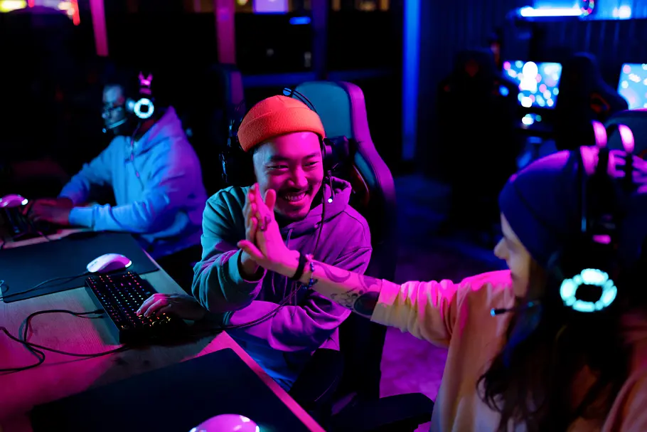 Die besten Games für eine Zock-Abend mit deinen Freund:innen Zwei Personen sitzen nebeneinander an Bildschirmen und geben sich High-Five.