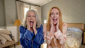 Man sieht Jamie Lee Curtis in einem blauen Pyjama und Lindsay Lohan in einem rosa Pyjama in einem Schlafzimmer stehen. Die beiden schauen entsetzt nach vorne. - Foto: IMAGO / Cinema Publishers Collection