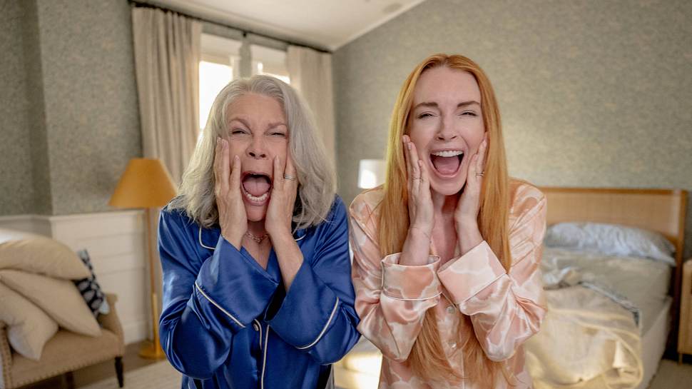 Man sieht Jamie Lee Curtis in einem blauen Pyjama und Lindsay Lohan in einem rosa Pyjama in einem Schlafzimmer stehen. Die beiden schauen entsetzt nach vorne. - Foto: IMAGO / Cinema Publishers Collection