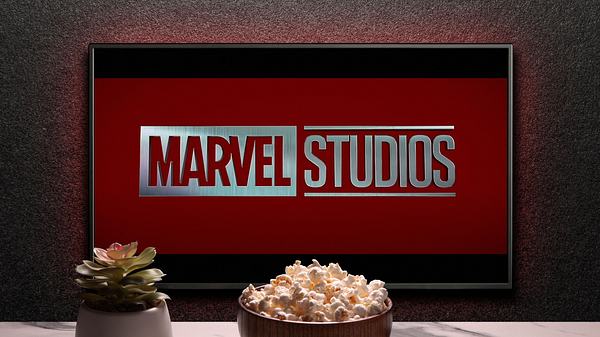 Man sieht einen Fernseher, auf dem „Marvel Studios“ steht. Vor dem Fernseher sieht man eine keine Pflanze, eine Schüssel mit Popcorn und eine Fernbedienung. - Foto:  IMAGO / Pond5 Images