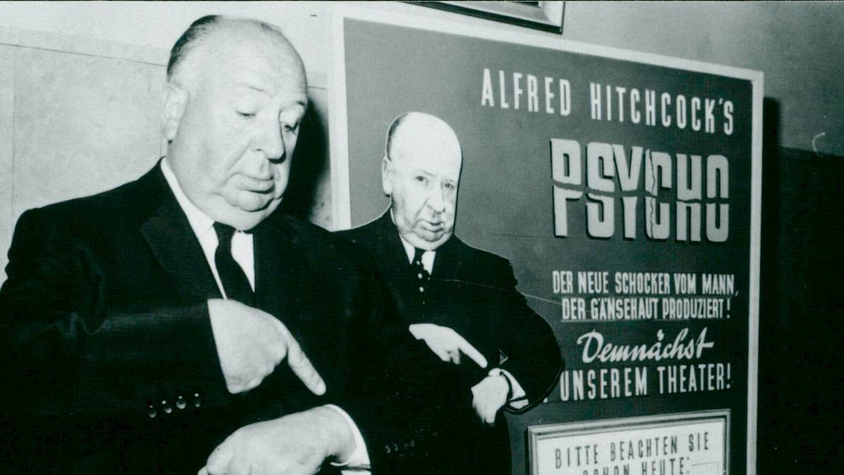 Alfred Hitchcock Alfred Hitchock steht vor einem Plakat von sich selbst und ahmt die Pose nach, die er auf dem Plakat macht. In dem Falle handelt es sich um ein Poster für den Film „Psycho“.