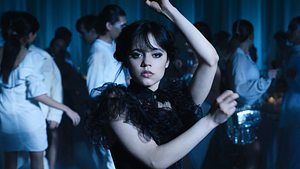 Wednesday Addams tanzt in einem schwarzen Kleid. Hinter ihr sind Personen in weißen Klamotten.  - Foto: COURTESY OF NETFLIX