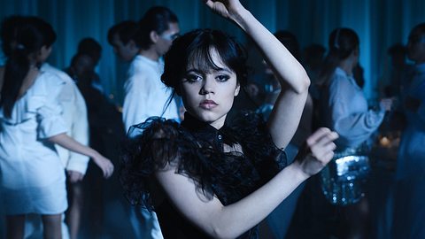 Wednesday Addams tanzt in einem schwarzen Kleid. Hinter ihr sind Personen in weißen Klamotten.  - Foto: COURTESY OF NETFLIX