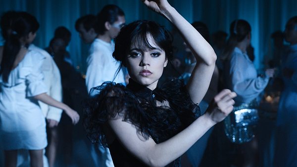 Wednesday Addams tanzt in einem schwarzen Kleid. Hinter ihr sind Personen in weißen Klamotten.  - Foto: COURTESY OF NETFLIX