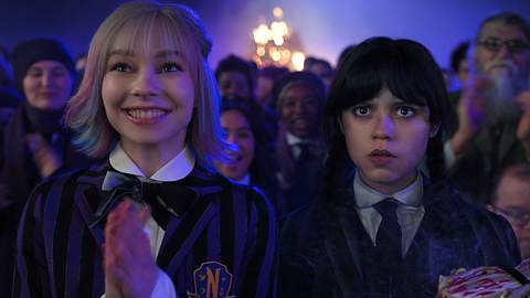 Emma Myers und Jenna Ortega in ihren Rollen als Enid und Wednesday aus der Netflix-Serie Wednesday. Enid schaut freudig und klatscht die Hände zusammen, während Wednesday mit einem mürrisch geschocktem Gesichtsausdruck neben ihr steht.  - Foto: Netflix